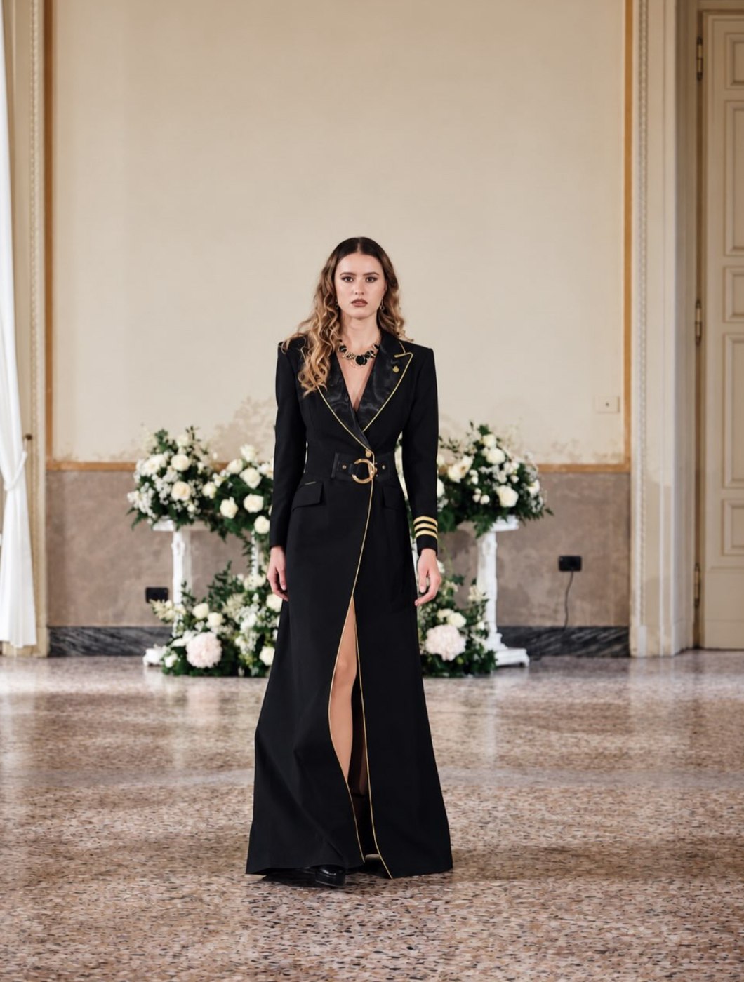 Black floor-length coat dress with gold piping, ring belt and thigh-high slit