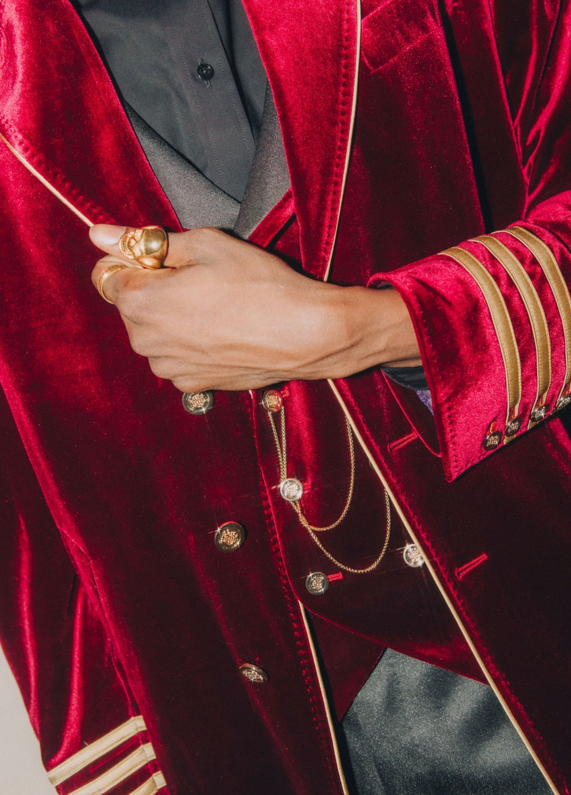 Close detail of a crimson velvet coat with gold buttons, chain and a gold ring
