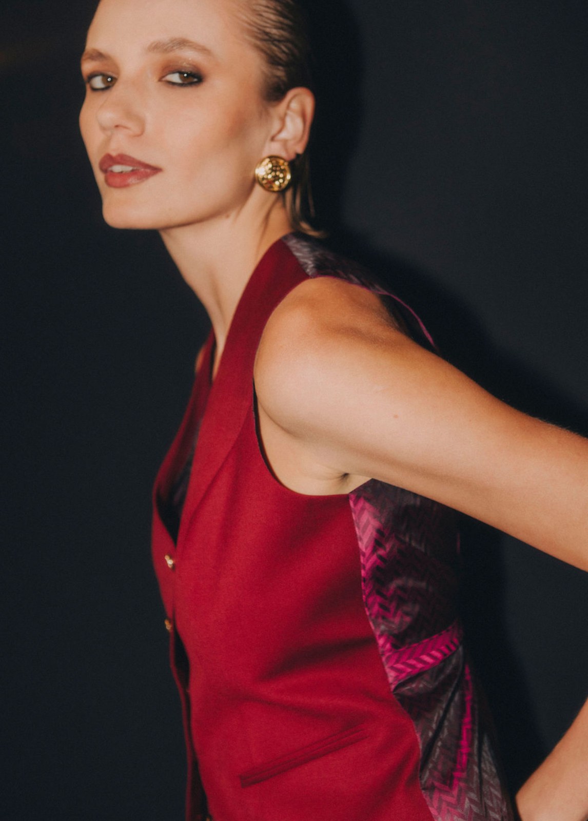 Model in a red waistcoat with a printed back and gold button earrings