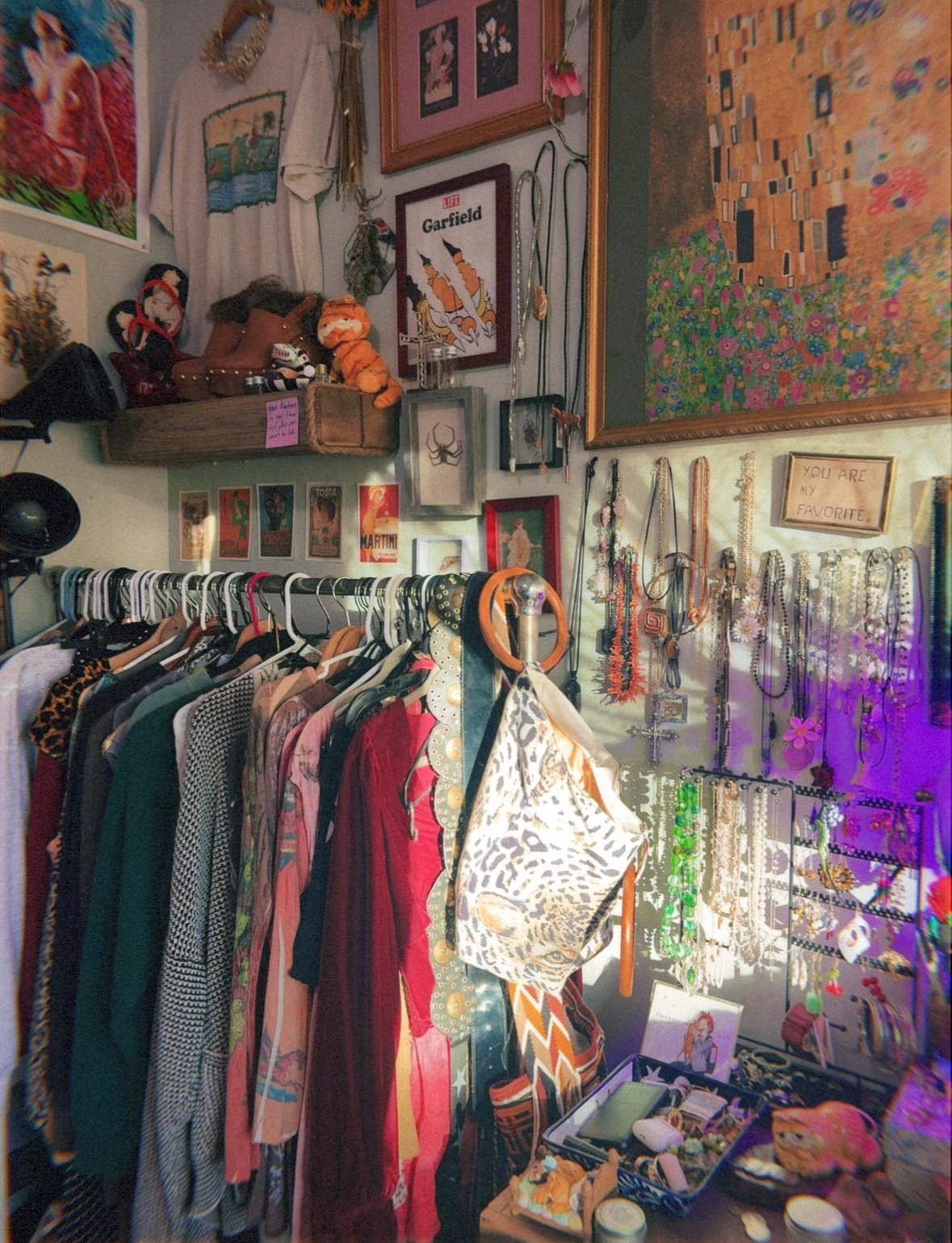 Isabella's own closet: a rack of vintage clothes, a wall of necklaces and earrings, framed art and boots on a shelf