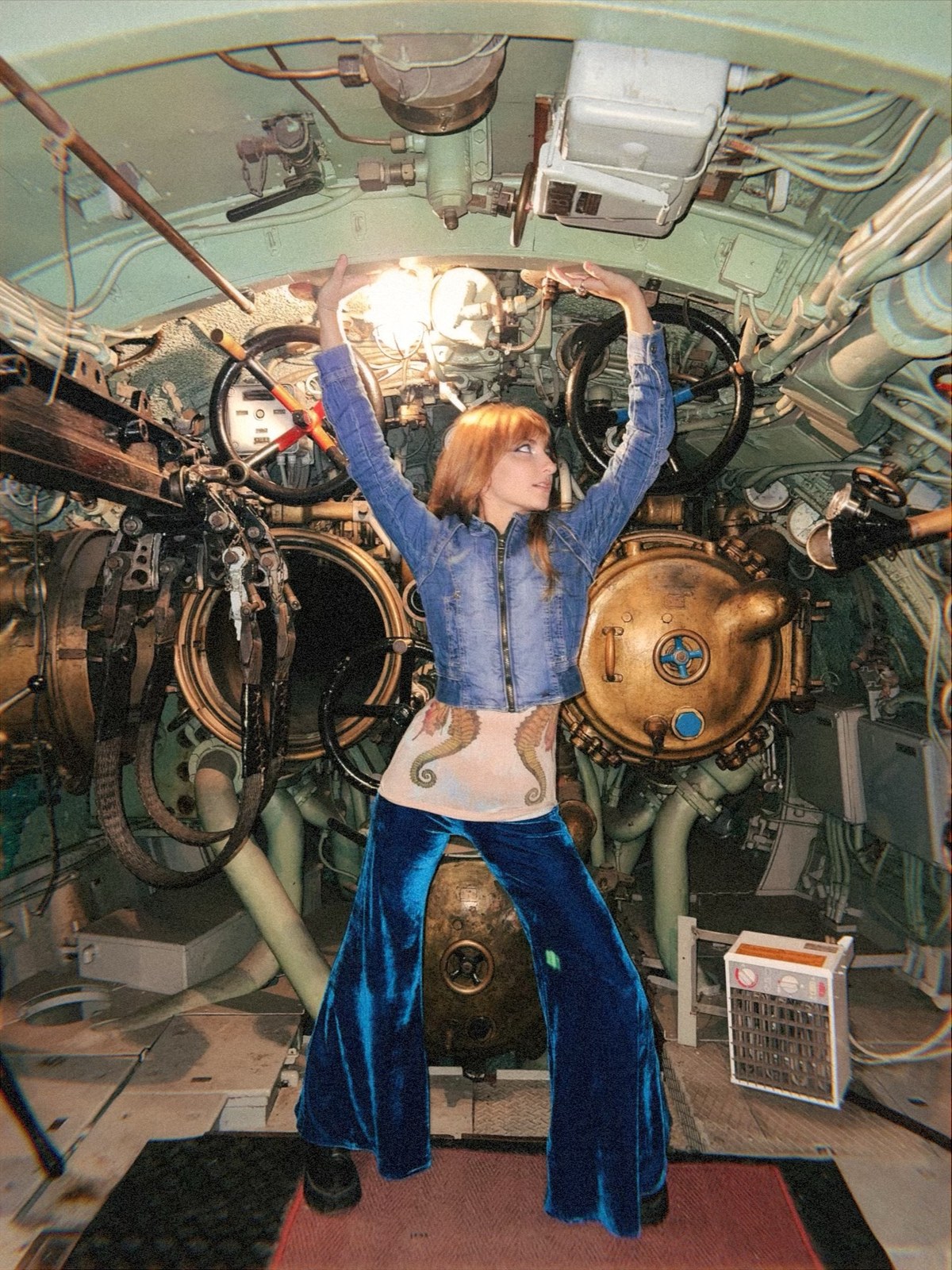 Isabella in a cropped denim jacket, seahorse top and blue velvet flares inside a submarine