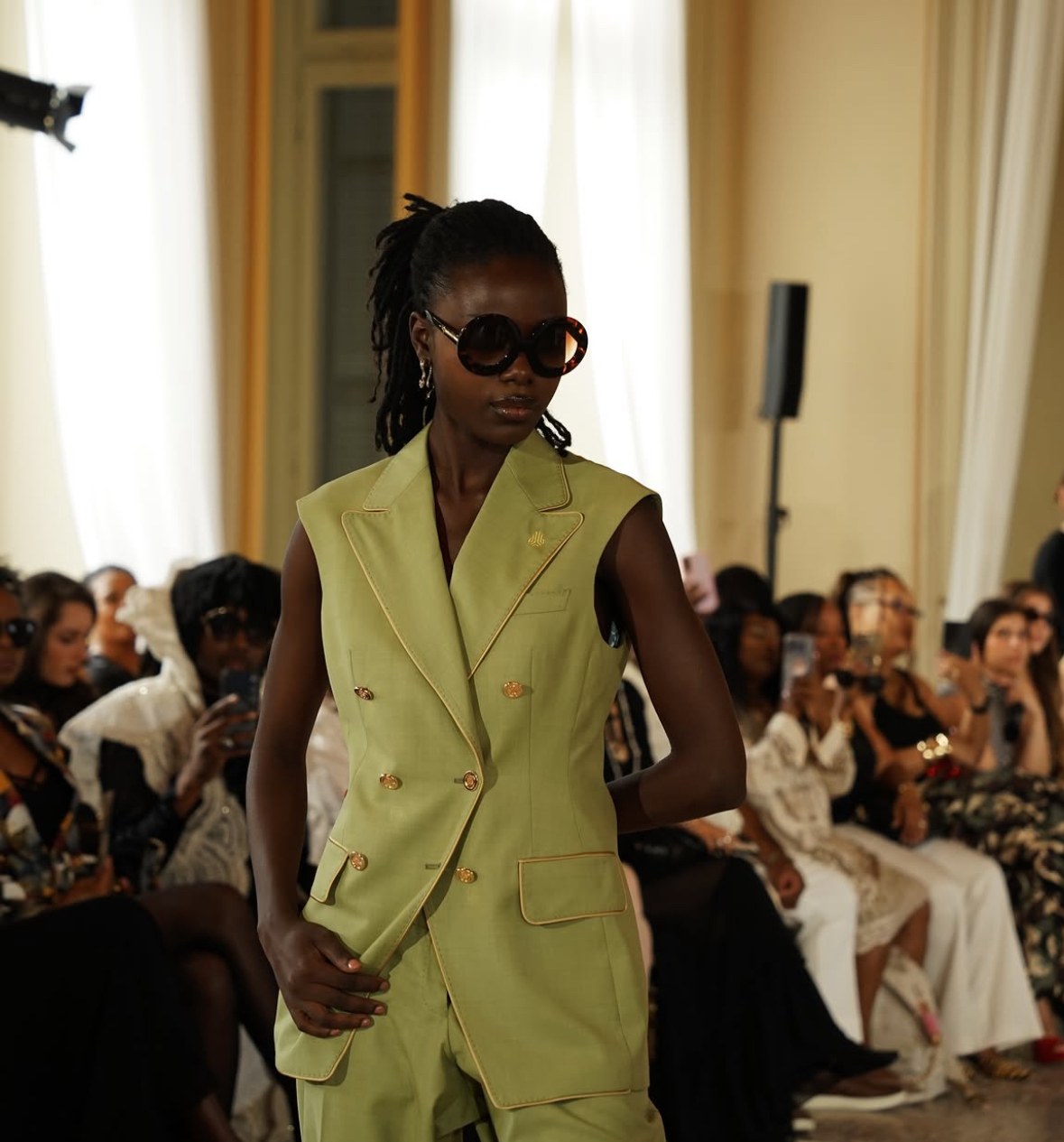 Model in a sage double-breasted DCASSO look with round tortoiseshell sunglasses