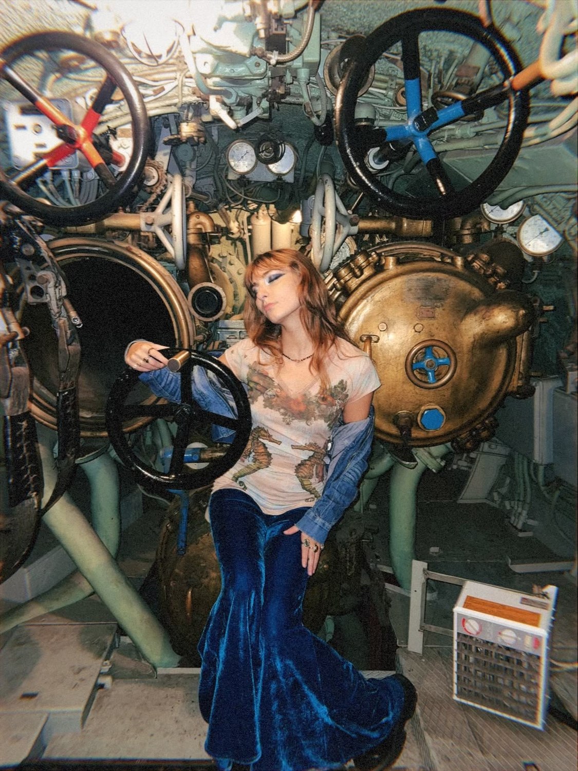 Isabella leaning against brass torpedo hatches, holding a valve wheel