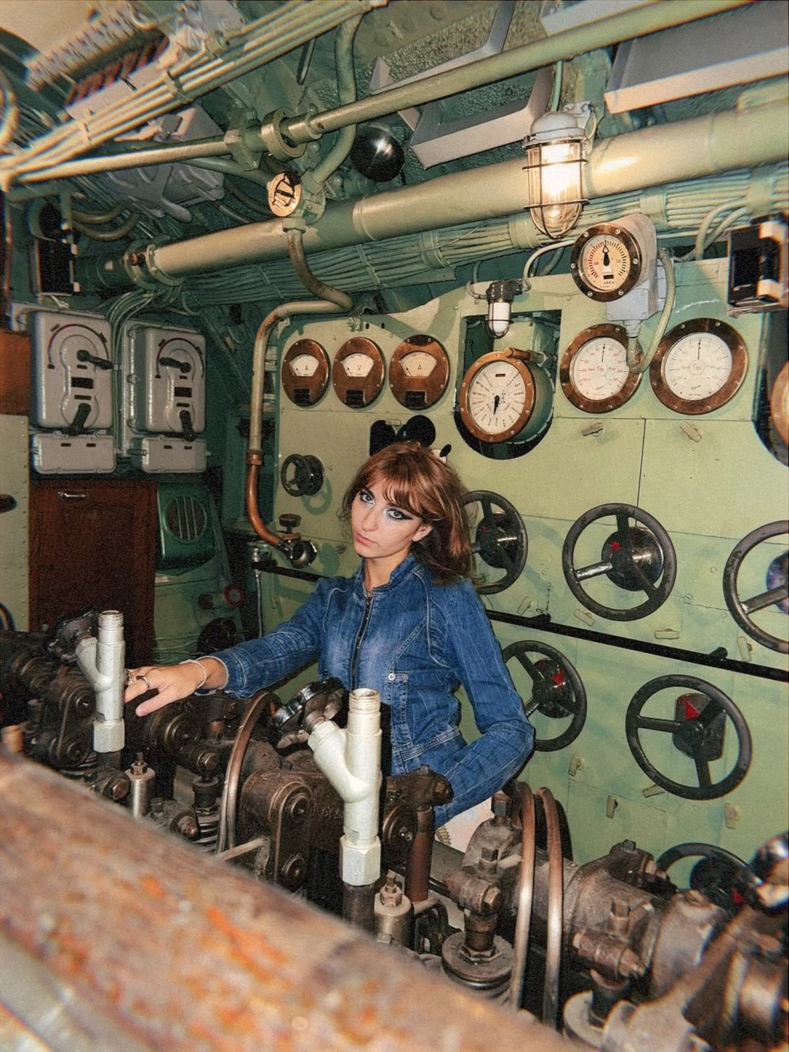 Isabella in a denim jacket at the submarine's control panel of gauges and valve wheels