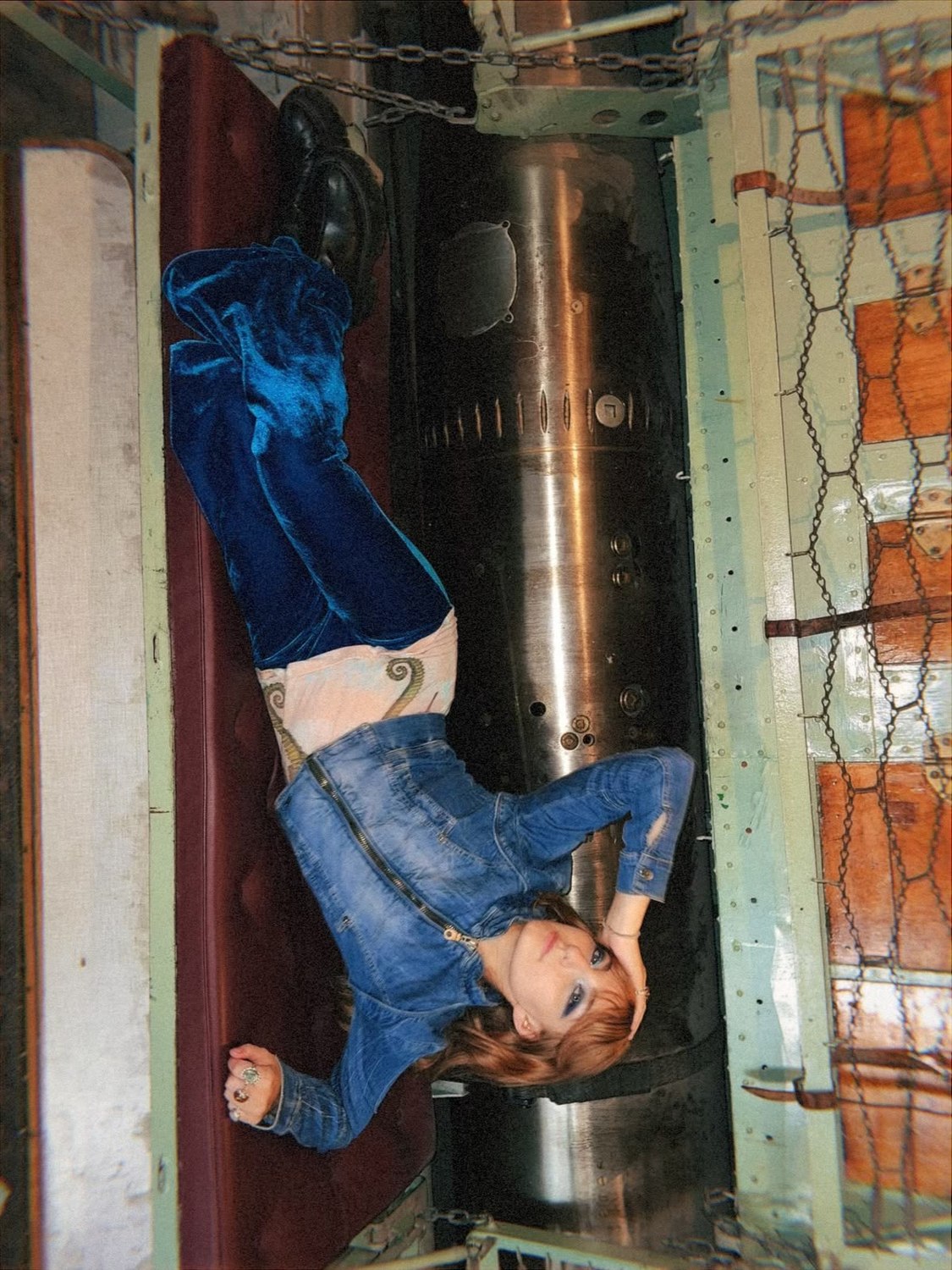 Isabella lying on a red bunk beside a torpedo, shot from above