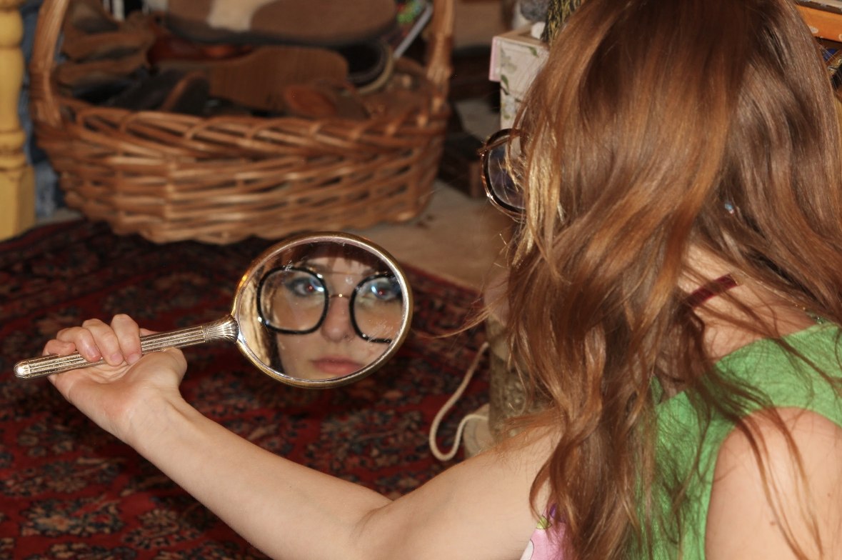 Isabella's reflection in a hand mirror, seen over her shoulder
