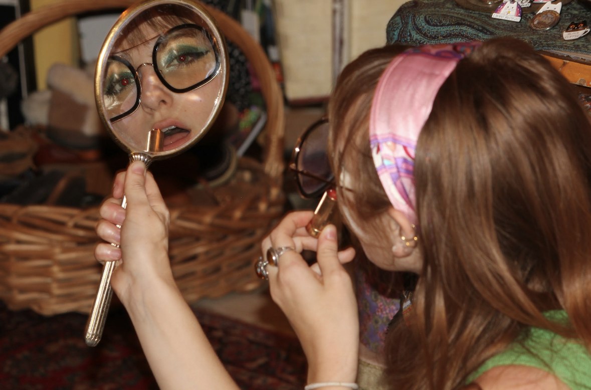 Isabella applying lipstick in a hand mirror