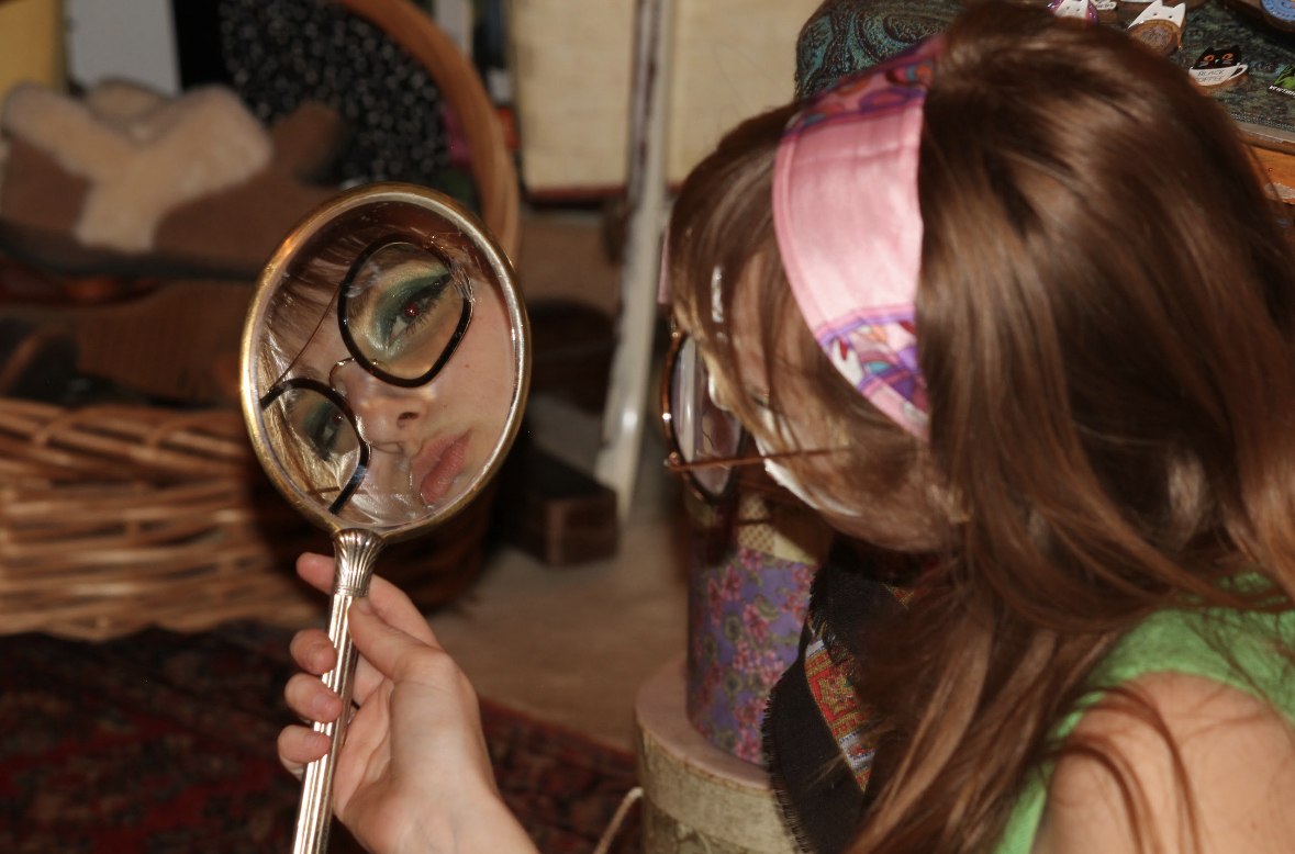 Isabella's reflection in a hand mirror wearing oversized glasses
