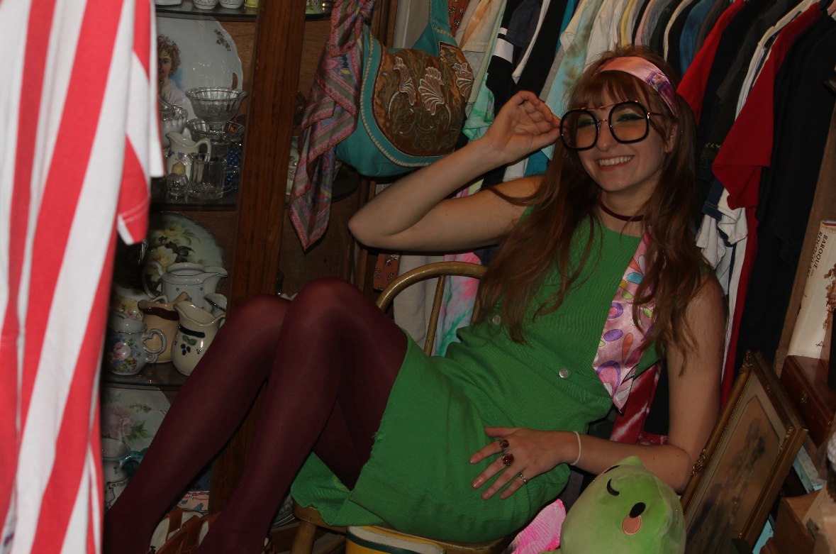 Isabella smiling in oversized glasses on a chair among clothing racks