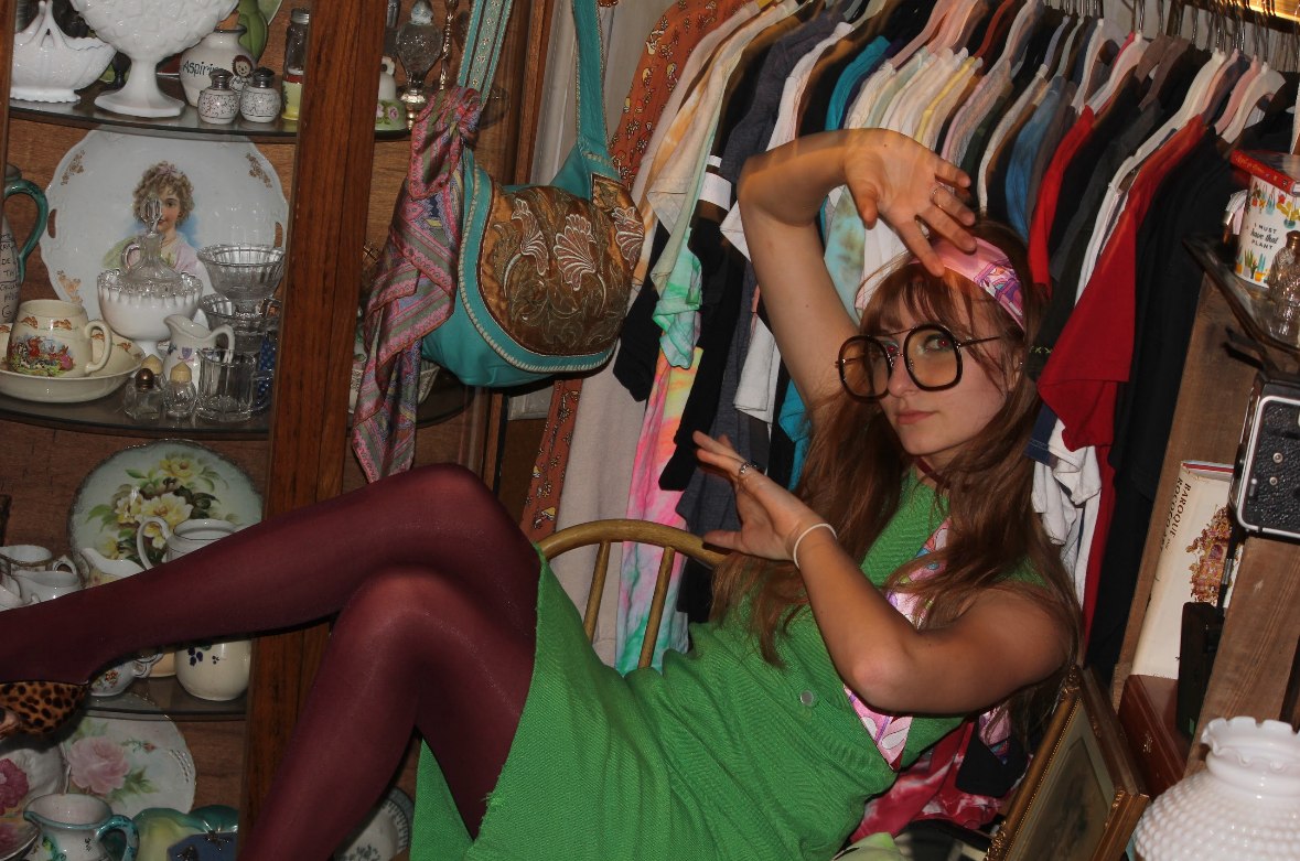 Isabella posing with raised hands on a chair among clothing racks