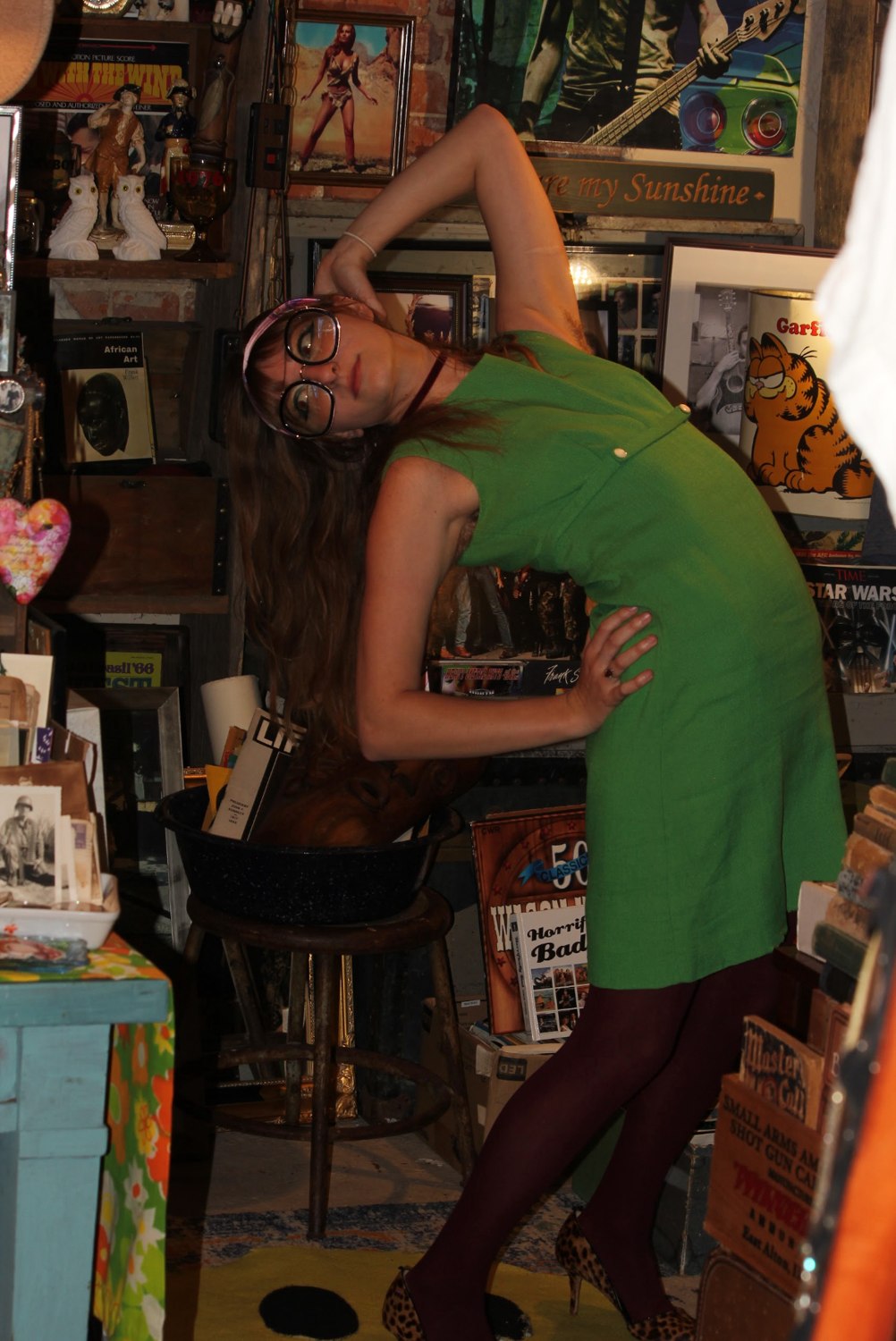 Isabella leaning back in a green shift dress among vintage posters